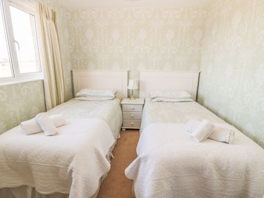 A bedroom with two single beds a nightstand with a lamp and a window at Baytree in Alnwick