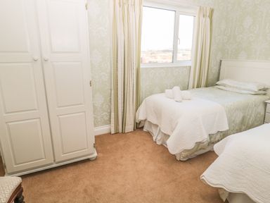 A bedroom with two single beds a wardrobe and a window with curtains at Baytree in Alnwick