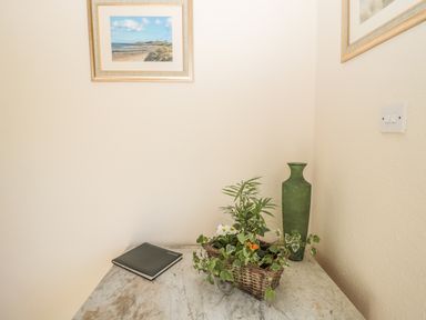A marble table with a black book a green vase and a basket with plants in a corner with two framed pictures on the walls at Baytree Alnwick