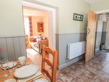 A dining table set with plates cups and glasses next to a wooden chair and an open door showing a living room at Baytree in Alnwick