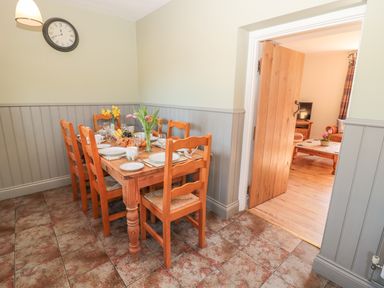 A dining area with a wooden table set for six and an adjoining room with a coffee table and television at Baytree in Alnwick