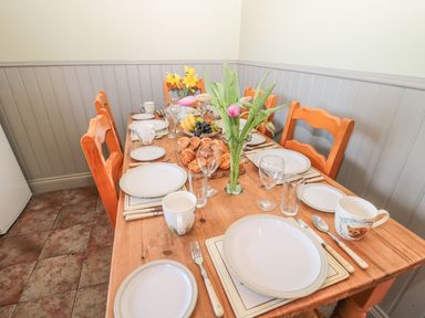 A dining table set with plates cups cutlery and glassware surrounded by wooden chairs with flowers and fruit on the table at Baytree in Alnwick