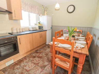 A kitchen with wooden cabinets a dining table set with plates cups and flowers and a refrigerator at Baytree in Alnwick