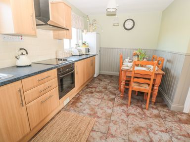 A kitchen with wooden cabinets a dining table with chairs and a clock on the wall at Baytree in Alnwick