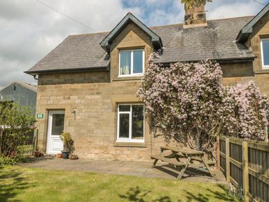 Exterior of stone cottage with a door and windows climbing plant and wooden picnic table at Baytree in Alnwick