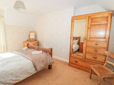 A bedroom with a wooden bed two rolled towels wooden wardrobe dresser with mirror and a wooden chair at Appletree in Alnwick
