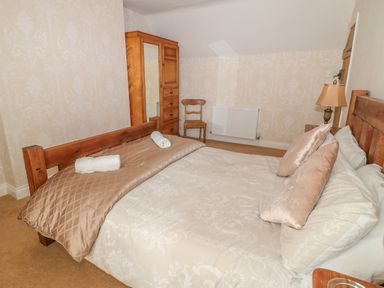 A bedroom with a wooden bed frame bedside lamp wardrobe and a chair at Appletree in Alnwick
