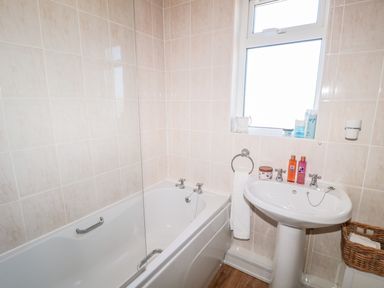 A bathroom with a bathtub a sink with toiletries and a window at Appletree in Alnwick