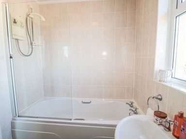 A bathroom with a bathtub with shower, a sink with toiletries, and a window at Appletree in Alnwick