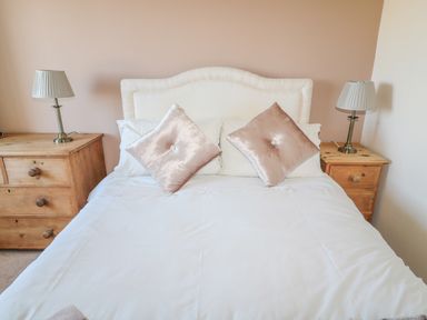 A bed with two pink pillows and white bedding between two wooden bedside tables with lamps at Appletree in Alnwick