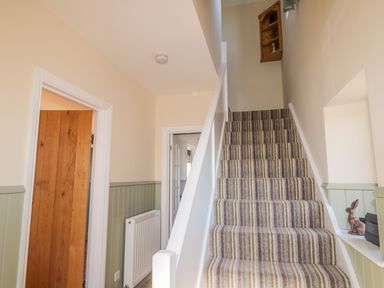A staircase with striped carpet next to a hallway with light green wall paneling at Appletree in Alnwick