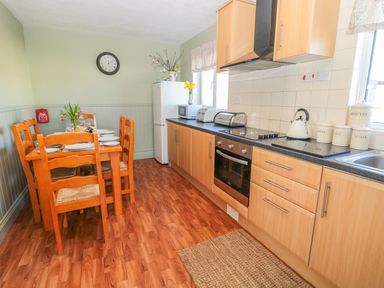 A kitchen with a wooden dining table set with plates and glasses next to wooden cabinets and appliances at Appletree in Alnwick