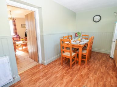 A dining area with a wooden table set with dishes and six chairs adjacent to a doorway leading to a living room at Appletree in Alnwick