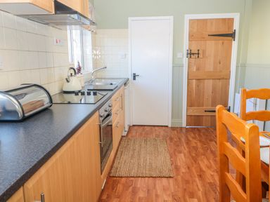 A kitchen with wooden cabinets black countertop electric stove white kettle sink wooden doors and wooden chairs at Appletree in Alnwick