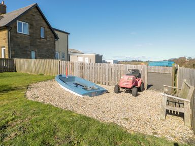 A garden area with a small boat a red ride-on mower a wooden bench and a fenced yard at Appletree in Alnwick