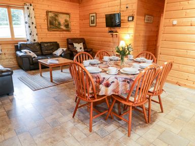 A dining table set with plates and cups next to a seating area with leather sofas and a wall-mounted television at Chloes Lodge in Middleton Ryedale