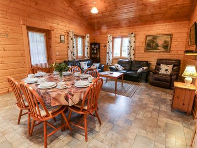 A dining area with a round table set for six and a living area with sofas and a coffee table at Chloes Lodge in Middleton Ryedale