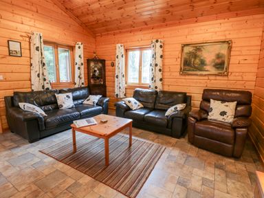 A living room with two black leather sofas a brown leather armchair wooden coffee table striped rug wood paneled walls and two windows at Chloes Lodge in Middleton Ryedale