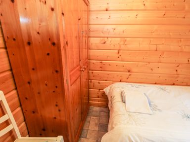 A bedroom with a wooden wardrobe a white chair and a bed with folded towels on it at Chloes Lodge in Middleton Ryedale