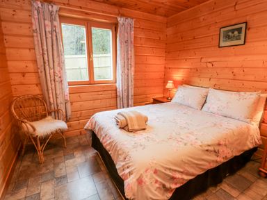 A bedroom with a double bed floral bedding a wicker chair and a window at Chloes Lodge in Middleton Ryedale