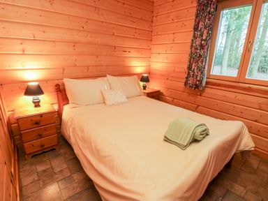 A bedroom with a bed and two bedside tables with lamps in a wooden cabin at Chloes Lodge in Middleton Ryedale