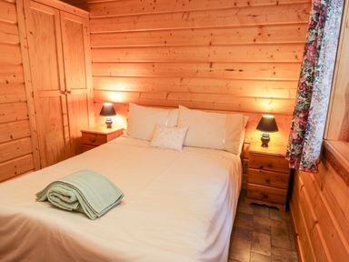A bedroom with a double bed between two wooden bedside tables with lamps in a wooden cabin at Chloes Lodge in Middleton Ryedale