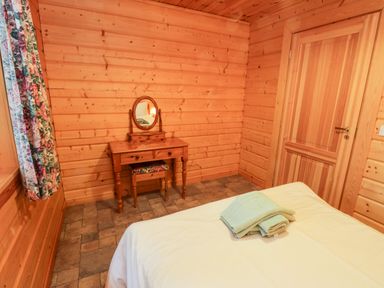 A bedroom with wooden walls a bed with towels on it a wooden dressing table with a mirror and floral stool at Chloes Lodge in Middleton Ryedale