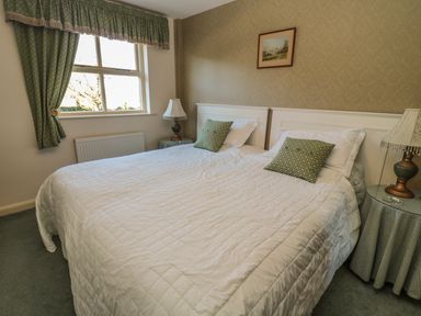 A bedroom with two single beds pushed together with white bedding green pillows two bedside tables lamps and a window with green curtains at Holly Cottage in Alnwick