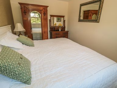 A bedroom with a bed white quilt green pillows a wooden wardrobe a dressing table with mirror and a wall mirror at Holly Cottage Alnwick