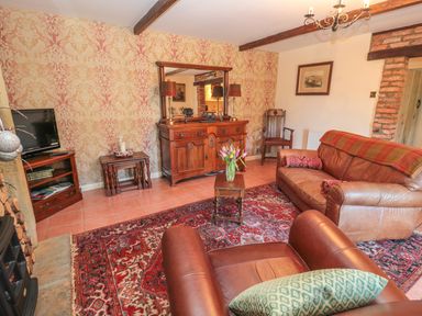 A living room with leather armchairs a sofa a wooden cabinet a television and a red patterned rug at Holly Cottage in Alnwick
