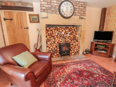 A living room with a leather armchair and a fireplace stacked with firewood at Holly Cottage in Alnwick