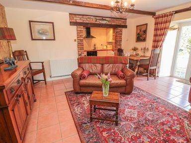 A living room with leather sofa wooden coffee table flowers on table dining table with chairs and kitchen visible through brick arch at Holly Cottage in Alnwick