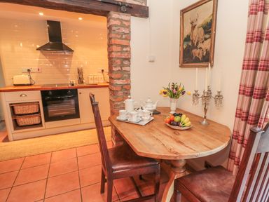 A small dining area with a wooden table set with a tea set and fruit bowl next to a kitchen with an oven and stovetop at Holly Cottage in Alnwick