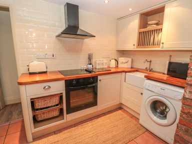 A kitchen with wooden countertops toaster stove washing machine and bread container at Holly Cottage in Alnwick