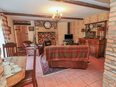 A living room with wooden beams a plaid throw on a sofa logs stacked in a fireplace and a wooden sideboard at Holly Cottage in Alnwick