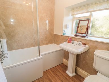 A bathroom with a bathtub a sink with toiletries a mirror and a toilet at Holly Cottage in Alnwick