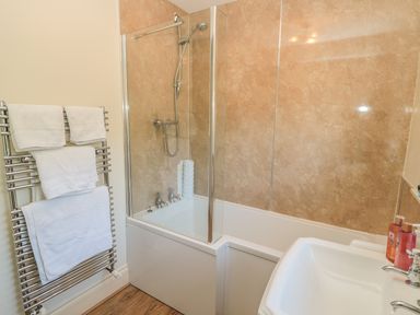 A bathroom with a bathtub shower combination towel rack with towels and a sink at Holly Cottage in Alnwick