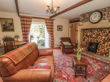 A living room with leather sofas a wooden coffee table and a fireplace with stacked logs at Holly Cottage in Alnwick