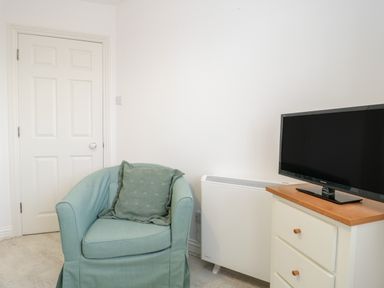 A room with a blue armchair next to a white heater and a chest of drawers with a television on top at 14 Lyme Mews in Seaton Devon