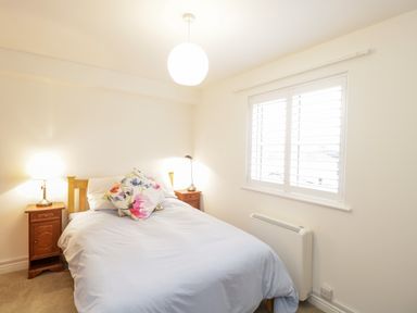 A bedroom with a double bed and floral cushions between two wooden bedside tables with lamps at 14 Lyme Mews in Seaton Devon