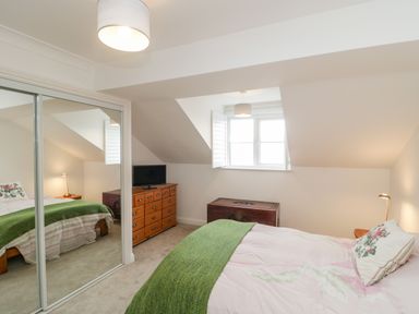 A bedroom with a bed a green blanket a dresser with a television a wooden chest and mirrored wardrobe doors at 14 Lyme Mews in Seaton Devon
