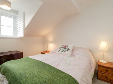 A bedroom with a bed covered with a pink duvet and a green throw next to two wooden bedside tables with lamps at 14 Lyme Mews in Seaton Devon