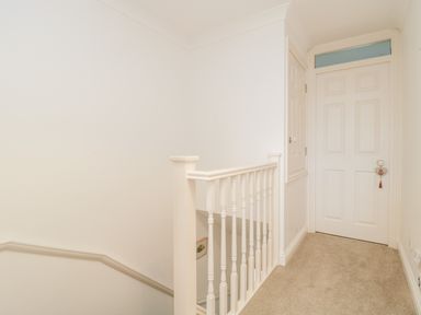 A hallway with carpet flooring a white banister and a closed white door at 14 Lyme Mews in Seaton Devon