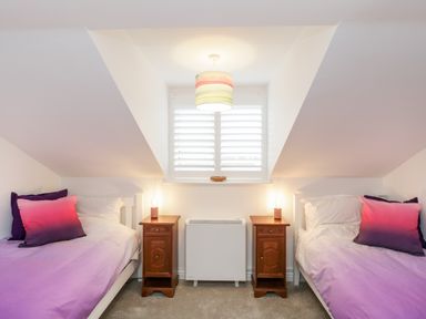 A bedroom with two single beds bedside tables lamps and a window with shutters at 14 Lyme Mews in Seaton Devon