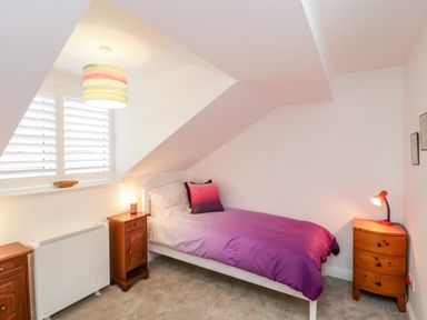 A small bedroom with a single bed and purple bedding next to wooden bedside tables with lamps at 14 Lyme Mews in Seaton Devon