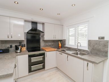 A kitchen with white cabinets grey countertops a black oven and stove a stainless steel sink and window with shutters at 14 Lyme Mews Seaton Devon