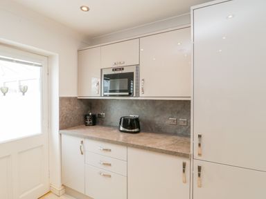 A kitchen area with white cabinets a microwave a toaster and a countertop at 14 Lyme Mews Seaton Devon