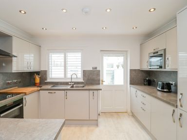 A kitchen with white cabinets a sink under a window a door opposite and various appliances at 14 Lyme Mews in Seaton Devon