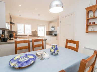 A kitchen with wooden chairs around a table with a blue tablecloth and colorful ceramics on it at 14 Lyme Mews in Seaton Devon
