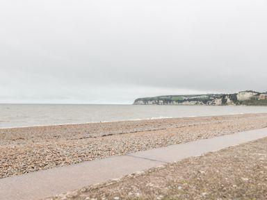 A pebble beach with a concrete walkway and sea cliffs in the distance at 14 Lyme Mews in Seaton Devon